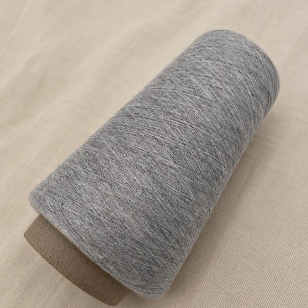 Cone sợi cotton melange chải kỹ màu xám đặt nghiêng trên nền vải
