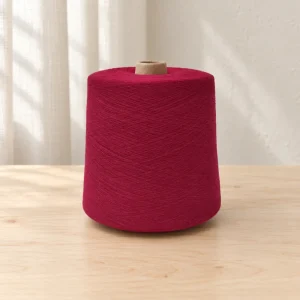 Cone sợi cotton nhuộm màu đỏ rượu vang Cone sợi cotton nhuộm màu đỏ rượu vang đặt trên mặt gỗ.